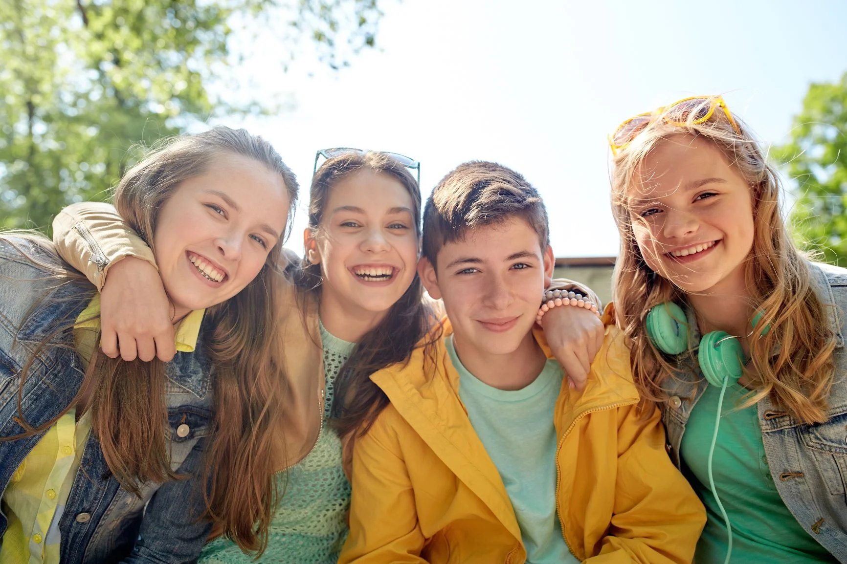 aocblog0519.jpg Four smiling teenagers pose together outdoors on a sunny day, wearing casual clothes and looking happy.