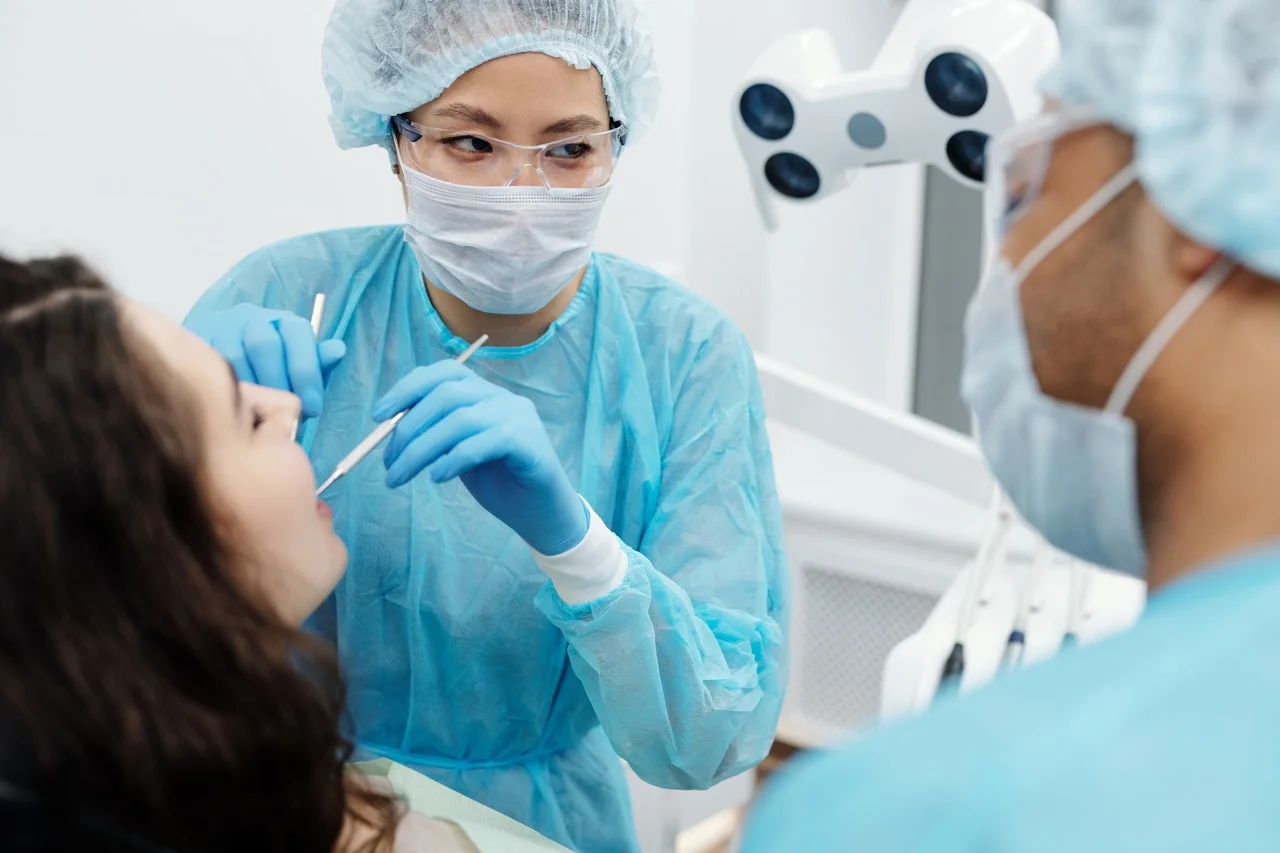 pexels-cedric-fauntleroy-4270940-1.jpg Dentist and assistant in masks and scrubs examining a patient’s mouth in a dental clinic.