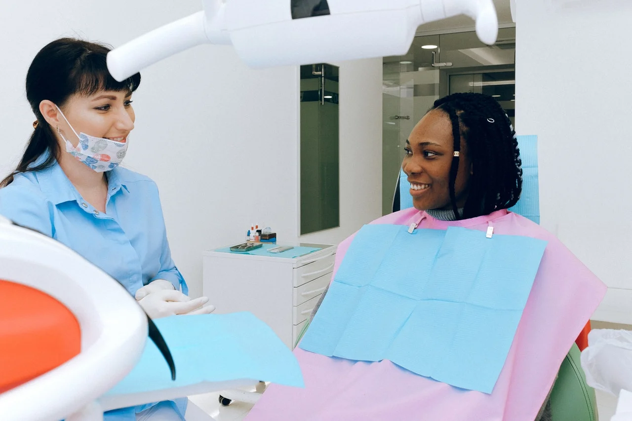 A dentist talks to a smiling patient in a dental clinic, both appearing friendly and relaxed.
