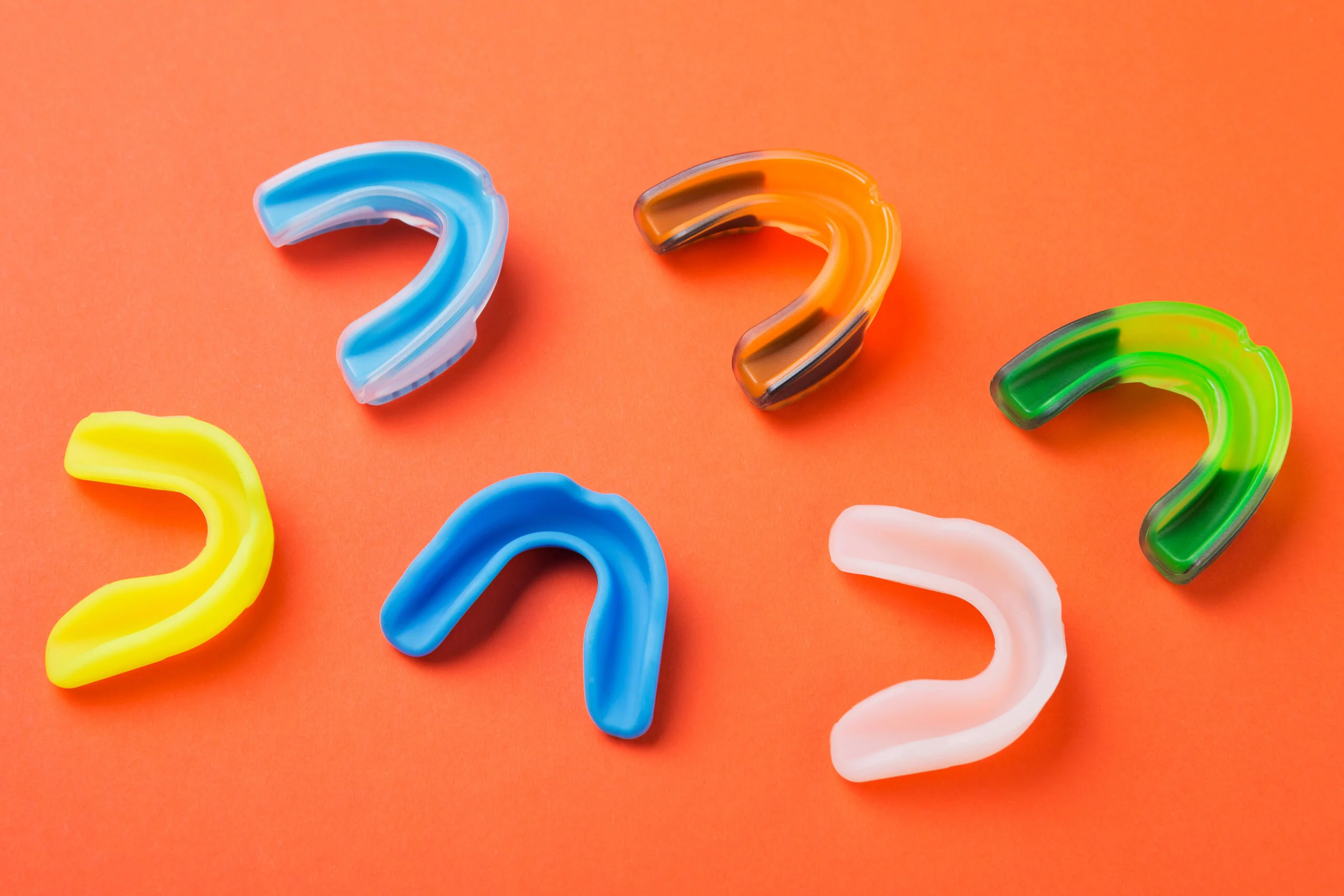 Six colorful mouthguards are arranged on an orange background.