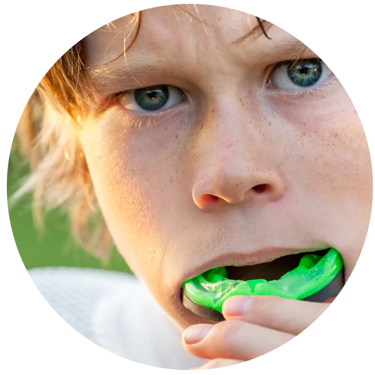 Close-up of a child with blue eyes putting a bright green mouthguard into their mouth.