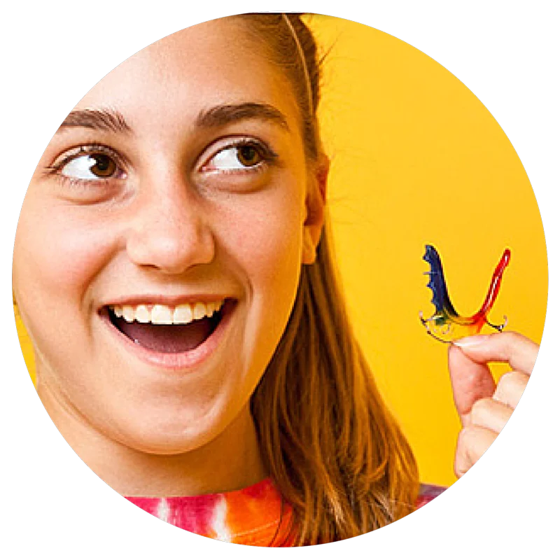 Smiling girl holding a colorful dental retainer against a bright yellow background.