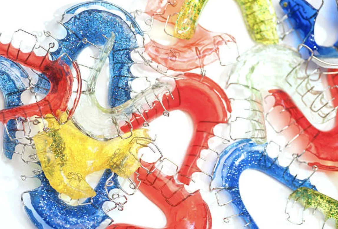 A pile of colorful orthodontic retainers, including red, blue, yellow, green, and glittery ones.