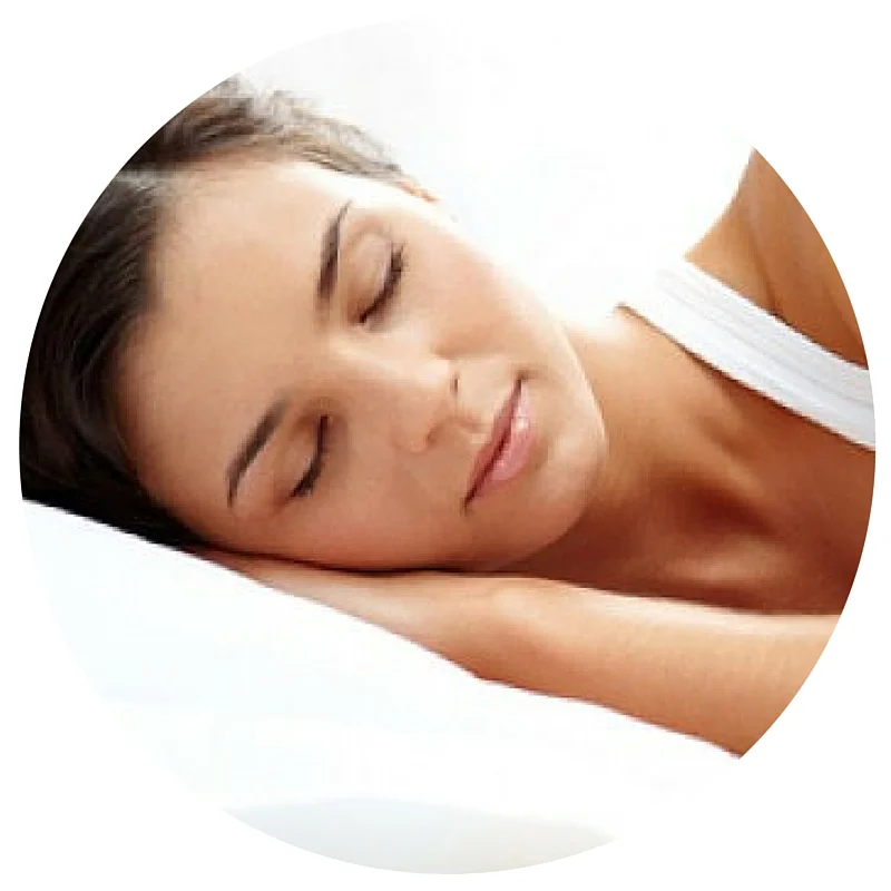 A woman with dark hair sleeps peacefully on a white pillow, wearing a white top.