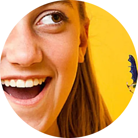 A smiling girl with an open mouth looks at a blue butterfly on a yellow background.