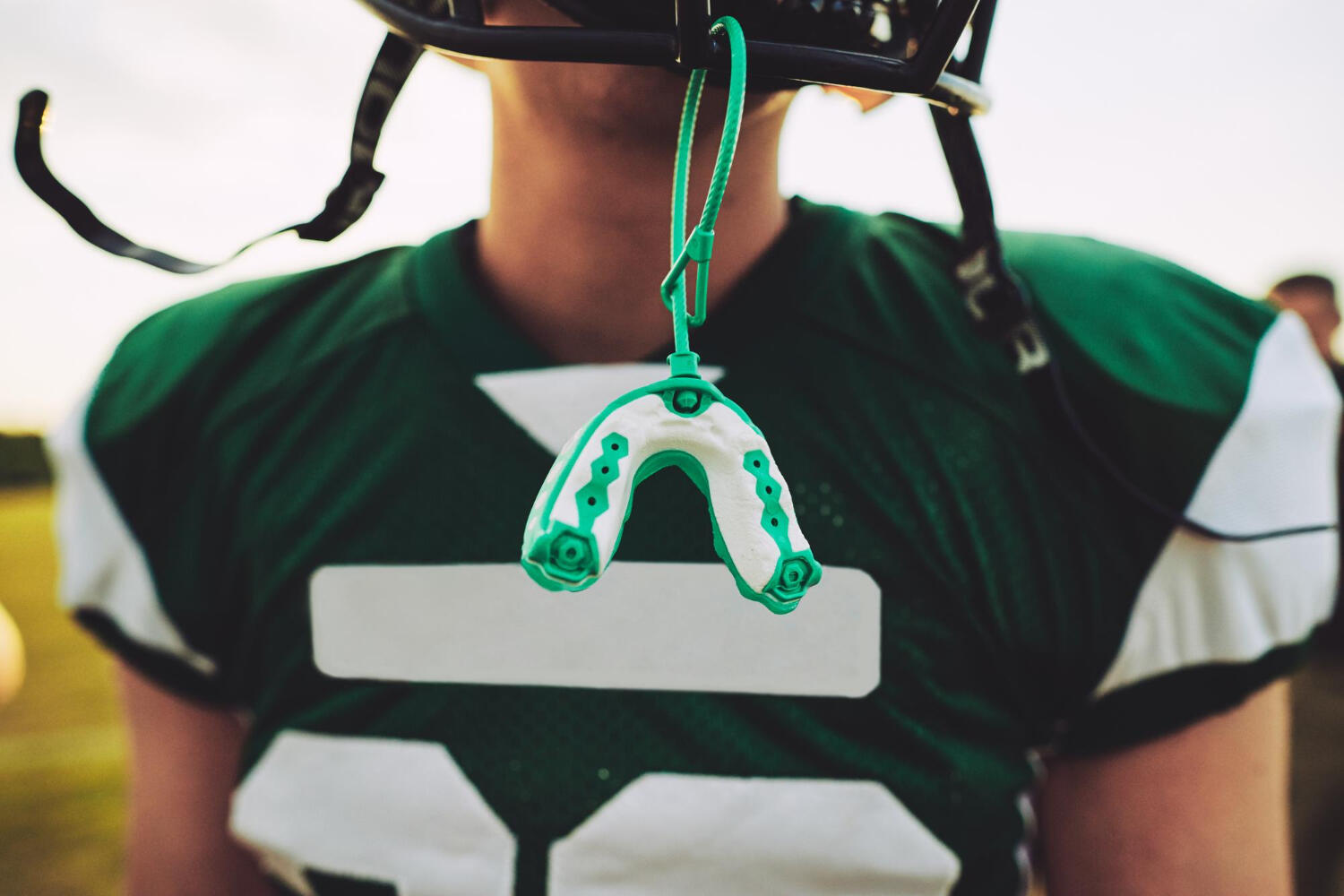 Close-up of a football player in green uniform with a mouthguard hanging from their helmet.